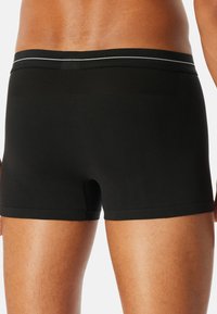 Pantaloni boxer neri realizzati in tessuto morbido, con una vestibilità aderente, una cintura larga con una striscia grigia e una texture soffice.