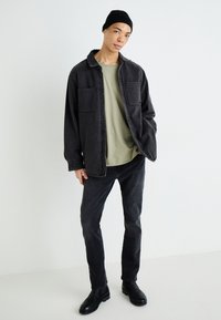 Tamsiai pilka džinsinė marškiniai su dviem krūtinės kišenėmis, dėvimi virš šviesiai žalio marškinio. Derinami su juodais džinsais ir juodais aulinukais, užbaigiami juoda beanie kepure.