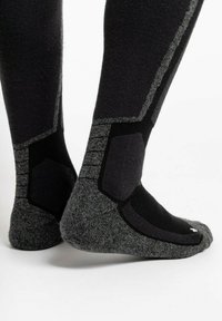 Schwarze und graue Socken mit einer strukturierten Oberfläche, die verstärkte Bereiche an der Ferse und den Zehen sowie kantige Designakzente an den Seiten aufweisen.