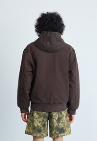 Felpa con cappuccio marrone dal taglio rilassato e con polsini a costine, abbinata a pantaloni corti verde militare con un motivo di stampa digitale.