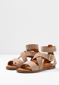 Sandalias de ante beige con correas superpuestas, puntera abierta, hebilla en el tobillo y una suela plana de madera. Acabado texturizado con acentos de hardware mínimos.