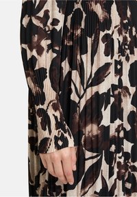 Blumenmusterkleid mit schwarzem Grund und beige- sowie braunfarbenen Tönen. Gefältelte Textur an den Ärmeln und fließendes Design. Weicher Stoff.