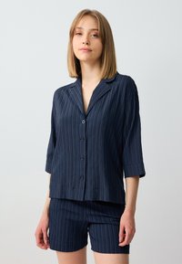 Set di abbigliamento loungewear blu navy composto da una maglietta a maniche corte con colletto e pantaloni corti abbinati, entrambi con un motivo ribbato e strutturato.