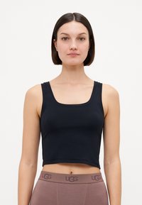 Black cropped tank top with thick straps and a square neckline, made from a smooth fabric. Paired with light brown high-waisted leggings.