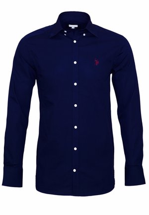 Námořnická modrá košile s dlouhým rukávem vyrobená z bavlny, s knoflíkovým zapínáním, špičatým límcem a malým červeným logem na levé části hrudi. Klasický střih a hladká textura.