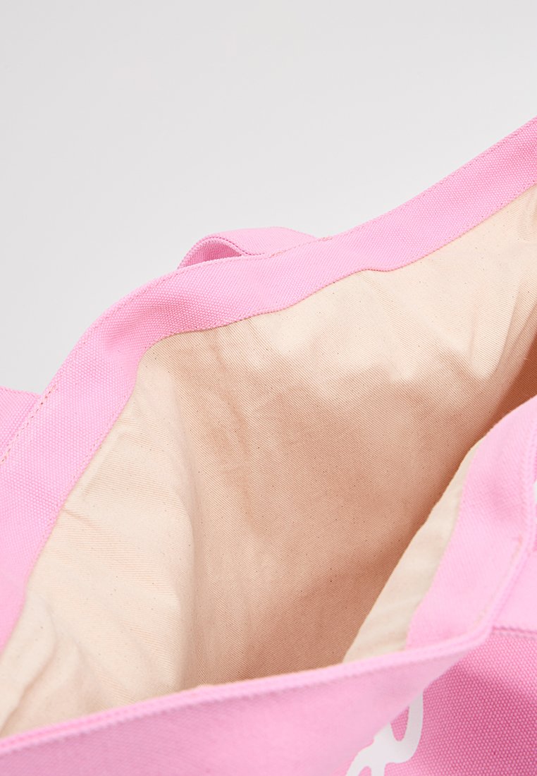 Sac fourre-tout en toile rose ouvert avec un intérieur en tissu beige et de larges poignées rose sur un fond uni.