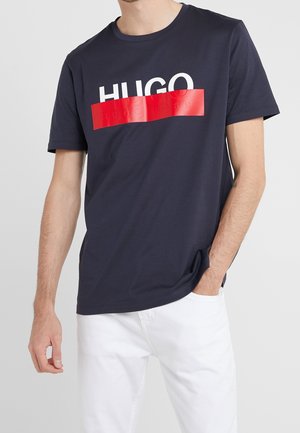 Navy blue cotton t-shirt featuring a bold red rectangular design with the text "HUGO" in white on the front. Short sleeves and crew neck.