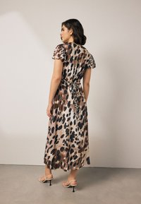 Vestito lungo con stampa leopardata caratterizzato da maniche corte a sbuffo, vita arricciata con una cintura e tessuto liscio e fluente in tonalità marroni.
