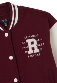 Bordeaux varsityjack met witte mouwen, voorzien van een textuur witte letter "R" en bedrukte tekst, ronde hals en drukknoopsluiting.