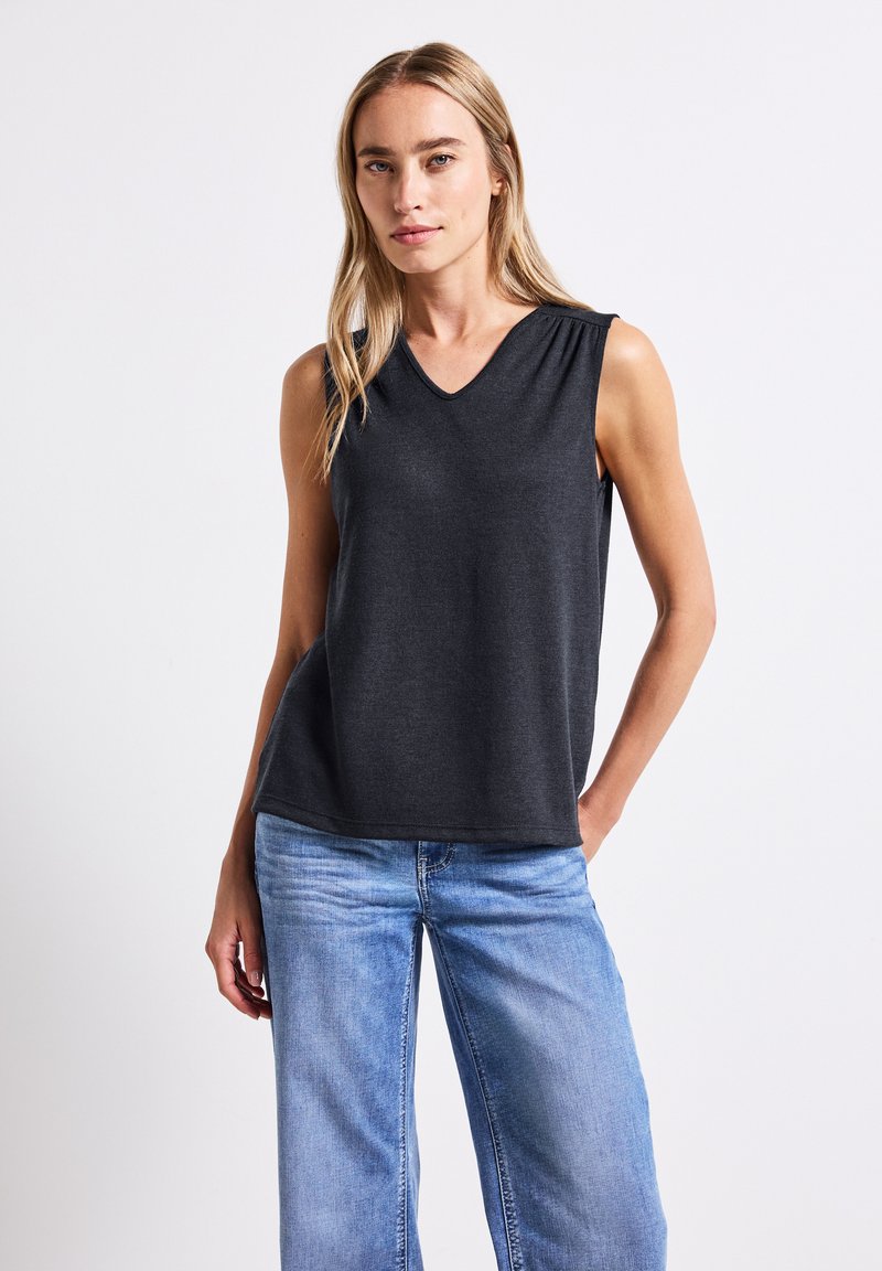 Top senza maniche grigio scuro con scollatura a V, realizzato in un materiale morbido. Abbinato a jeans in denim a gamba larga blu chiaro.