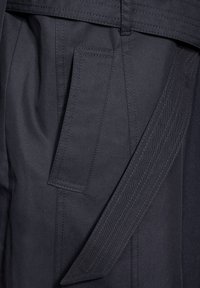 Granatowy materiał z dużą, płaską kieszenią z widocznymi szwami. Zawiera pasek z wbudowanymi pętelkami i gładką strukturą.