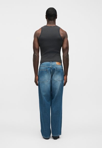 Μαύρο αμάνικο τοπ και μπλε τζιν παντελόνι με φαρδιά μπατζάκια και ξεθωριασμένο πλύσιμο. Διακριτικές πίσω τσέπες και δερμάτινο ταμπελάκι στη μέση.