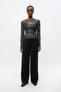 Black, wide-leg trousers paired with a sheer, fitted, long-sleeve top featuring a subtle, soft texture and varying green tones.