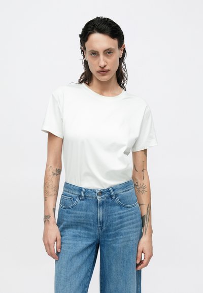 Άσπρο βαμβακερό μπλουζάκι με κοντά μανίκια και στρογγυλή λαιμόκοψη, συνδυασμένο με ανοιχτό μπλε τζιν παντελόνι ψηλής μέσης με εμπρόσθιες τσέπες και κούμπωμα με κουμπιά.