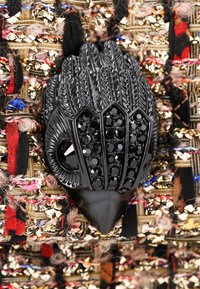 Spilla nera a forma di mano con texture simile a piume e accenti di cristallo, su uno sfondo di tessuto multicolore a motivi.