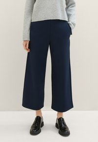 Marintröjor i bred benstil av ett mjukt, lätt tyg med sidofickor, i kombination med en grå ribbad tröja och svarta snörskor.