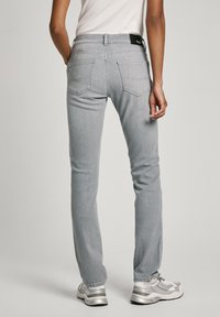 Pantalones vaqueros de mezclilla gris con corte slim, diseño de cinco bolsillos y etiqueta en la cintura negra, combinados con zapatillas deportivas plateadas.