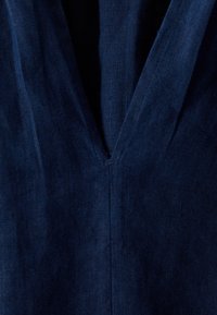 Tessuto di lino blu navy con un design a V-scollo, presenta una cucitura verticale centrale e un piccolo apertura all'collo. Finitura testurizzata.