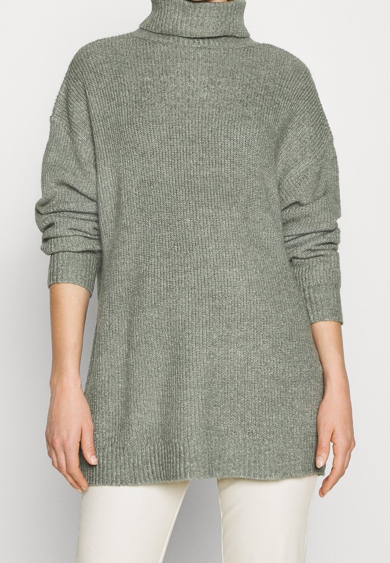 Jersey de cuello alto verde de punto con mangas largas y un corte relajado. Los puños y el dobladillo acanalados añaden textura a la prenda.