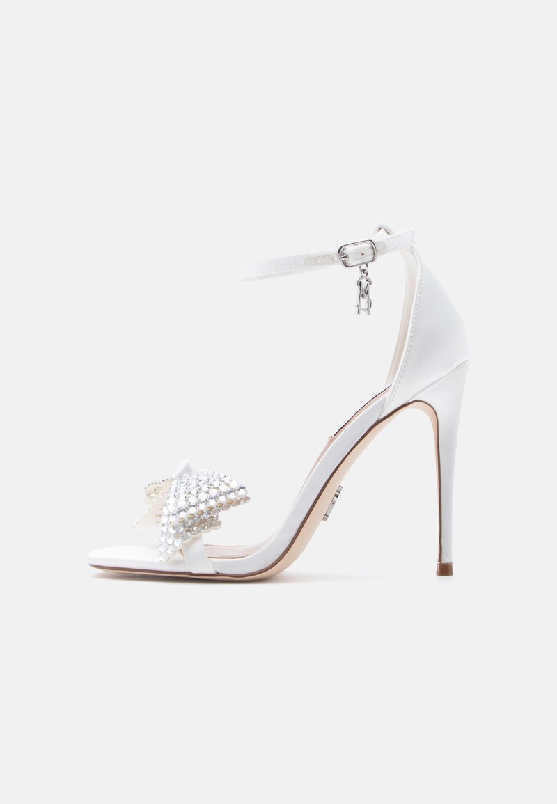 Άσπρο γυναικείο πέδιλο με ψηλό τακούνι και λουράκι στον αστράγαλο, διακοσμημένο με στρας στο λουράκι των δακτύλων και μικρό κρεμαστό στολισμό στη αγκράφα.