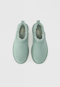 Πράσινες μποτάκια αστραγάλου από σουέντ με λεία υφή, στρογγυλεμένη μύτη, μαλακή επένδυση από γούνα και πίσω λουρί για εύκολη εφαρμογή. Επίπεδη ελαστική σόλα.