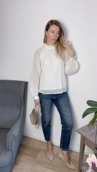 Blusa branca com bolinhas, com mangas bufantes, combinada com jeans azuis e saltos beiges. Os acessórios incluem uma pequena bolsa bege.