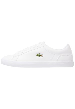Hvid lavtop sneaker med snøredesign og lille grønt krokodillelogo på siden, mod en ensfarvet hvid baggrund.