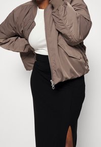 Khaki bomber bunda s ribovanými manžetami, zipem a bočními kapsami, spárovaná s těsnou černou sukní s rozparkem na stehně.