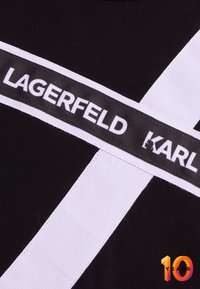 Tessuto nero con strisce orizzontali e verticali bianche. Presenta un'etichetta con la scritta "LAGERFELD" e "KARL" in un testo audace e a contrasto.