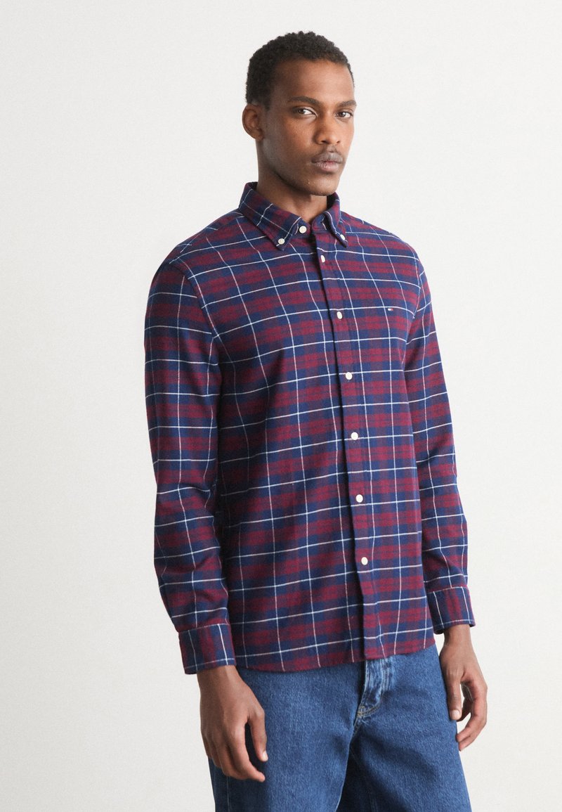 Camisa de cuadros roja y azul marino con cuello abotonado, mangas largas y botones blancos; textura suave con un corte relajado.