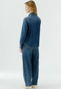 Jeansjacke und Jeans mit weitem Bein in Dunkelblau, mit klassischem Kragen, Knopfmanschetten und sichtbaren Nahtdetails auf dem Stoff.