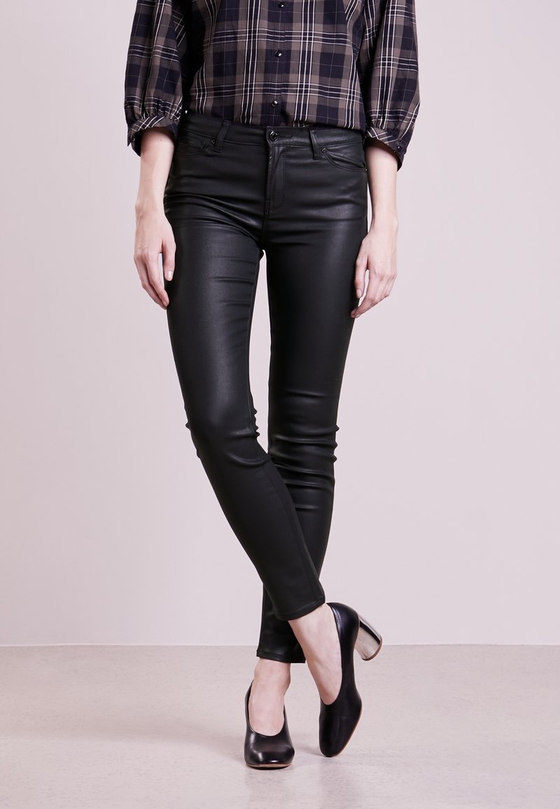 Svarta byxor i faux läder med slim fit och en slät yta, kombinerade med en rutigt blus och svarta klackskor.