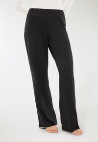 Pantaloni neri a gamba larga realizzati in un tessuto liscio ed elastico con una vita elasticizzata. Presentano un taglio a lunghezza piena e nessun motivo o accento visibile.