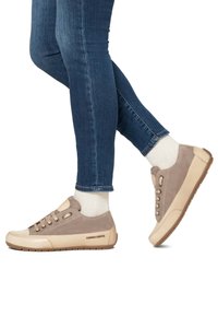 Beige semišové a kožené tenisky se světlou špičkou, s tkaničkami a gumovou podrážkou, nošené s modrými džíny a světlými ponožkami.