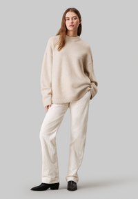 Beige oversized trui met geribde halslijn, gecombineerd met crèmekleurige corduroy broeken en zwarte enkellaarsjes. Soepele textuur met een ontspannen pasvorm.