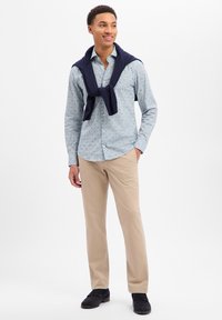 Jasnoniebieska koszula na guziki z wzorem, spodnie khaki, granatowy sweter zarzucony na ramiona oraz ciemne mokasyny. Prosty, nowoczesny design.