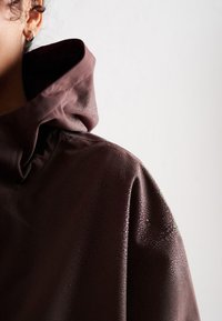 Chaqueta con capucha en burdeos de textura suave, con un acabado repelente al agua y sutiles gotas de humedad en la tela.