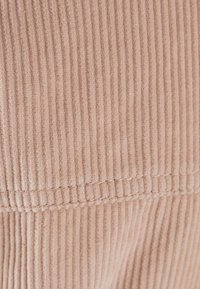 Tessuto di velluto a coste rosa chiaro con texture a righe verticali e dettagli di cucitura ben rifiniti. Morbido al tatto, adatto per diversi capi di abbigliamento.