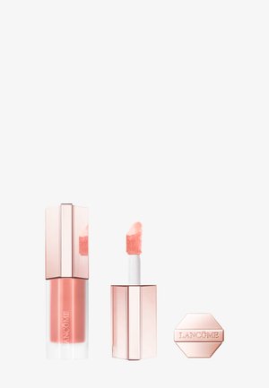 Gloss à lèvres dans un tube transparent rose avec un applicateur texturé et duveteux. Présente un design géométrique épuré et des accents argentés sur l'emballage.