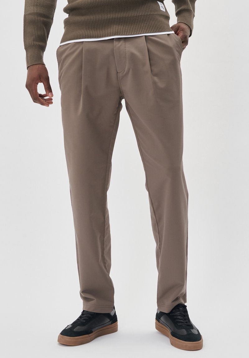 Khaki plisované kalhoty, lehký materiál, volný střih, kapsy po stranách, kombinované s černými teniskami a texturovaným hnědým svetr.