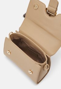 Beige leren handtas met een gestructureerde vorm, gouden hardware en knoopsluiting. Het interieur heeft een ritsvak en een gladde voering.