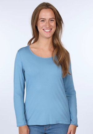 Helles blaues Langarmshirt in lockerer Passform mit rundem Ausschnitt und dekorativem Besatz entlang des Kragens und der Ärmel, kombiniert mit Jeans.