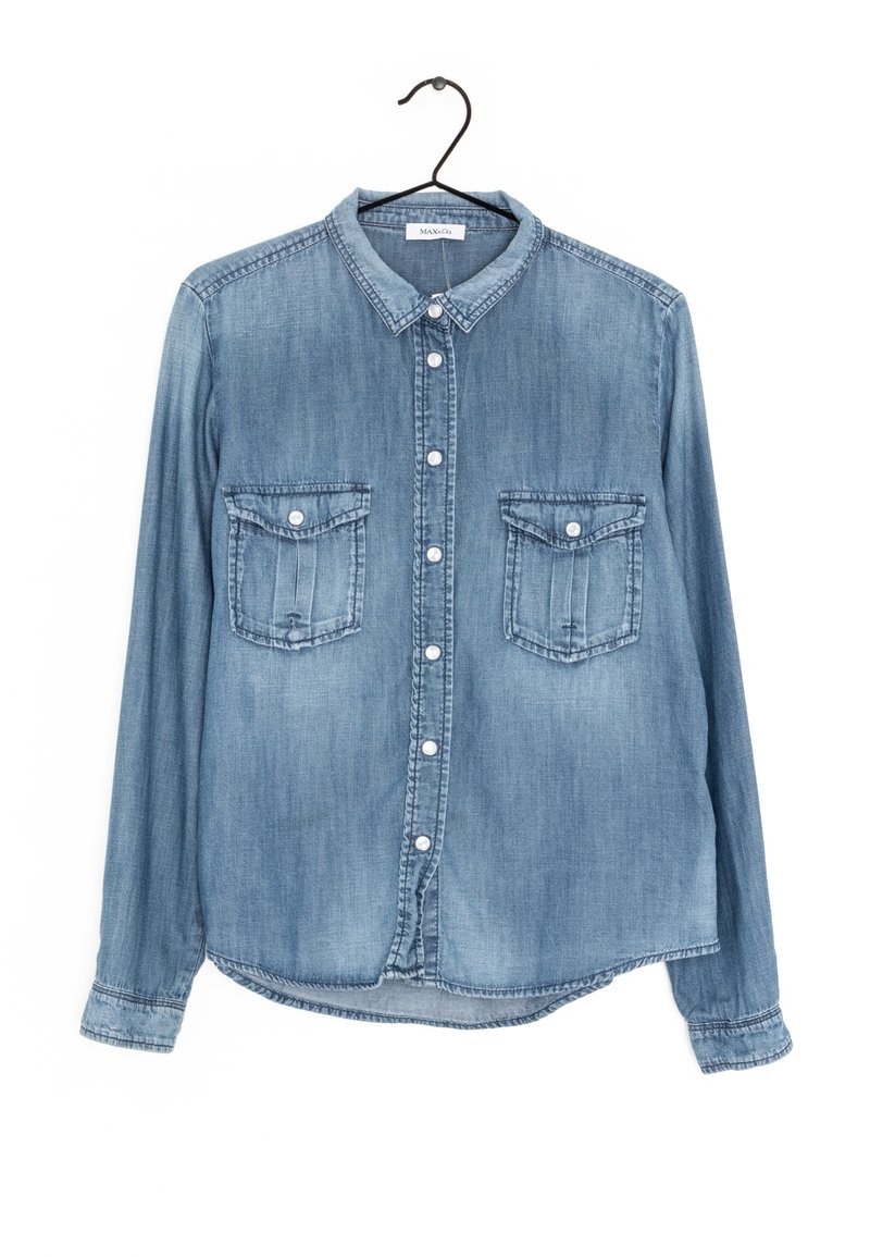 Camicia in denim con maniche lunghe, colore azzurro chiaro, chiusura frontale con bottoni, due tasche sul petto e colletto classico. Tessuto morbido con dettagli cuciti.