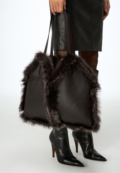 Borsa tote in pelle marrone con rifiniture in pelliccia scura, dotata di doppi manici. Presenta una texture liscia e una forma strutturata e angolare.