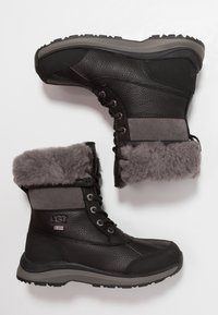 Czarne skórzane zimowe buty z szarym futrem wewnętrznym, sznurowane z przodu, z wytrzymałymi szarymi podeszwami, pokazane z widoków bocznych i od spodu.
