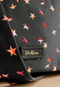 Tessuto nero con motivi di stelle multicolori in rosso, rosa e arancione. Presenta un'etichetta nera con cuciture dorate, che recita "Cath Kidston."