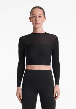 Top cropped negru cu mâneci lungi, cu un design ajustat; material neted cu secțiune superioară transparentă. Combinate cu colanți negri cu talie înaltă.
