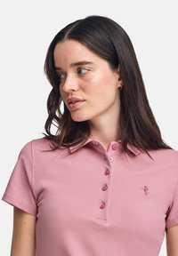 Rosa polotröja i strukturerad bomull, med krage, korta ärmar och en knapplist med fem knappar i matchande färg. Broderad logotypdetalj.