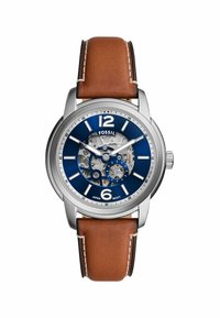Montre Fossil avec un boîtier en acier inoxydable argenté, un cadran bleu, un mouvement transparent, et un bracelet en cuir marron avec des coutures blanches.