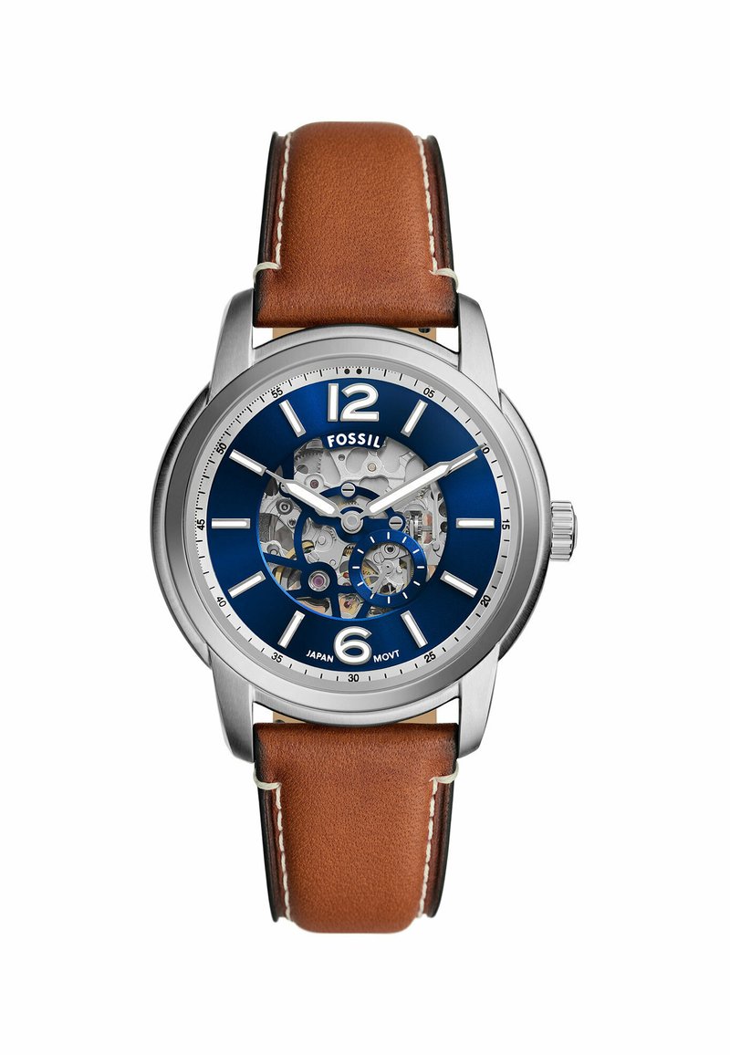 Montre Fossil avec un boîtier en acier inoxydable argenté, un cadran bleu, un mouvement transparent, et un bracelet en cuir marron avec des coutures blanches.